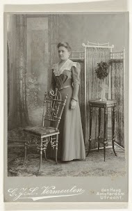 Studioportret van een vrouw in een lange jurk bij een kamerscherm