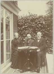 Twee mannen en een vrouw zittend bij een huis met een boek op tafel