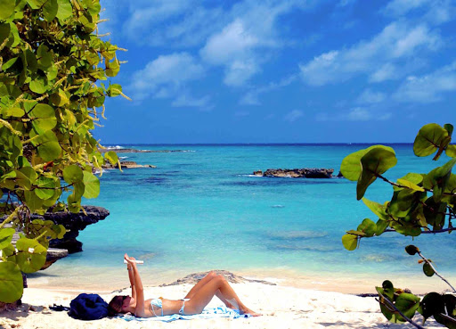 A woman reads while sunbathing along the azure shoreline of Smith Cove on Grand Cayman Island.