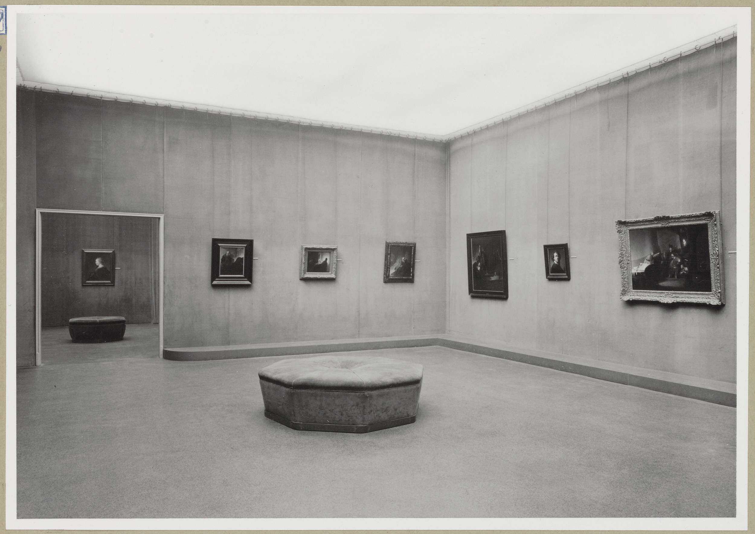 Zaal met zes schilderijen en een doorkijk naar een schilderij in een andere zaal links