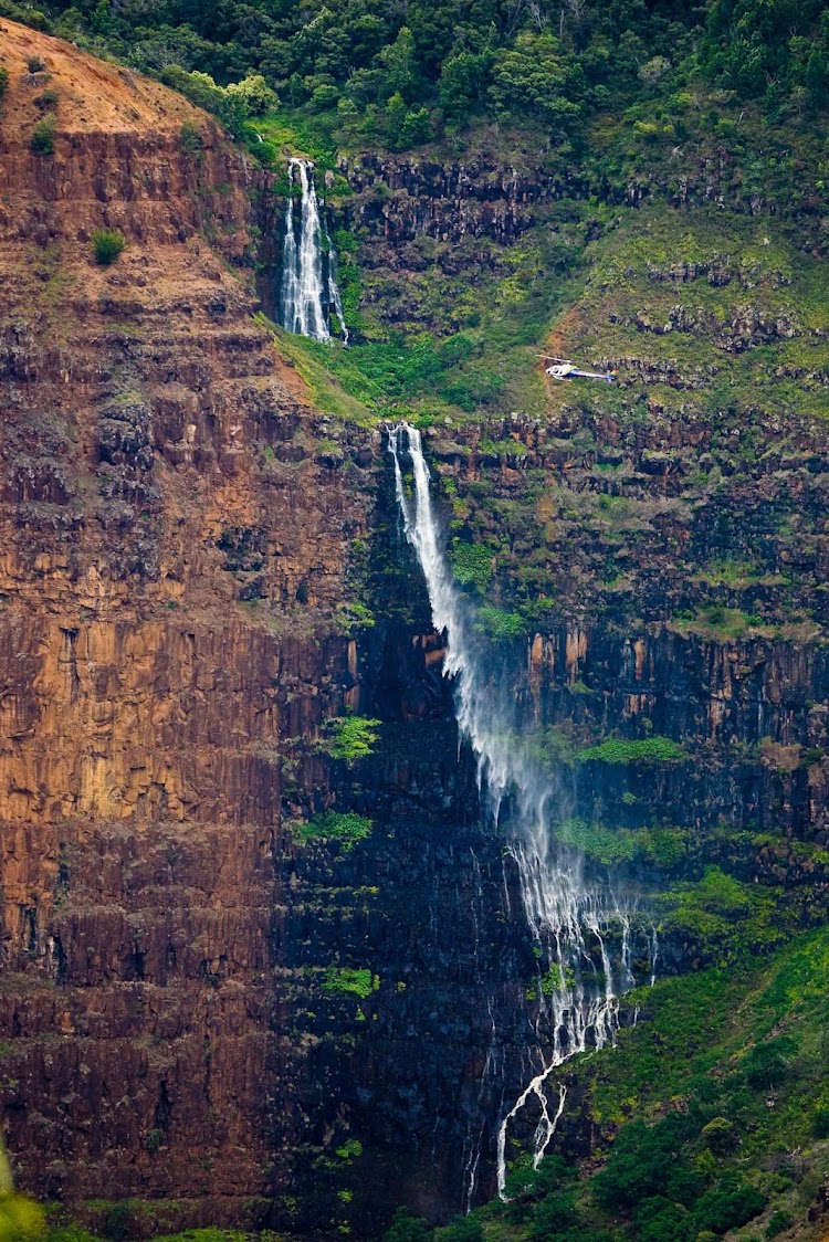 A waterfall in Waimea Canyon, known as the Grand Canyon of the Pacific, on the western side of Kauai viewed from a helicopter.