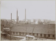 Exterieur van fabrieksgebouwen met schoorstenen, op de voorgrond houten vaten