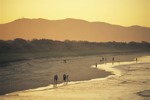 People stroll along the beach at sunset at Hat Head, near South West Rocks, Kempsey, North Coast, New South Wales, Australia.