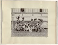 Vrouwen zittend en staand voor een huis met balen op het hoofd in Nederlands-Indië