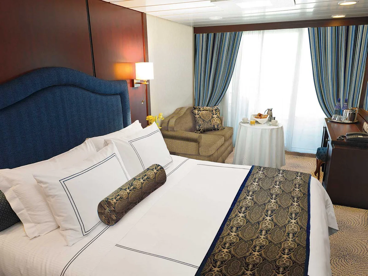 Oceania-B-Veranda-Stateroom - Oceania Nautica's Veranda stateroom offers a private teak veranda for taking in panoramic views, a queen bed with 1,000-thread-count linens, a vanity desk, refrigerated mini-bar, breakfast table and spacious seating area. It's located mid-ship on deck 6 and is 216 square feet.