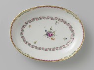Schaal, diep en ovaal van vorm,behorend bij een servies met geslingerd lintmotief met bladertakken, bloemboeketten en gestrooide bloemtakken