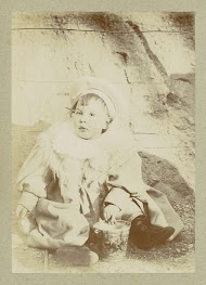 Portret van een jong kind met een jas, een sjaal en een muts, zittend bij een speelgoedemmer