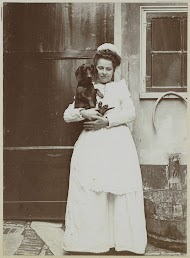 Dienstbode met een takshond in de armen bij een buitenkraan