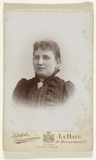 Studioportret van een dame met oorbellen in een zwarte jurk met opstaande kraag