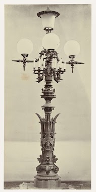 Lantaarn met vier glazen bollen en een glazen cilinder in het midden, omringd door een kandelaar, het geheel rust op een gedecoreerde bronzen standaard.