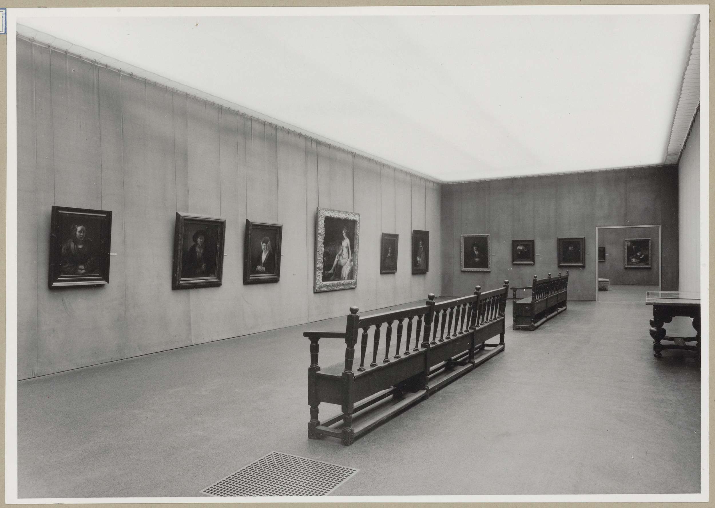 Zaal met negen schilderijen, rechts een tafel en achteraan een doorkijk naar een andere zaal