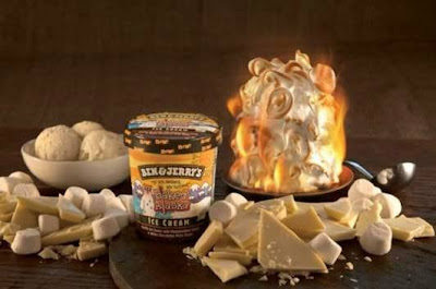 Tub of ben & Jerry's Ice cream on a table, surrounded by chocolate pieces, ice cream and a flaming baked alaska
