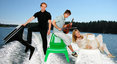 image shows three people with a lake and waterski-trails photoshopped into the background, while they're sitting on brightly neon coloured plastic chairs.