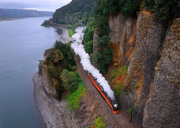 A steam train runs alongside the river and rock at Washougal, Washington, USA
