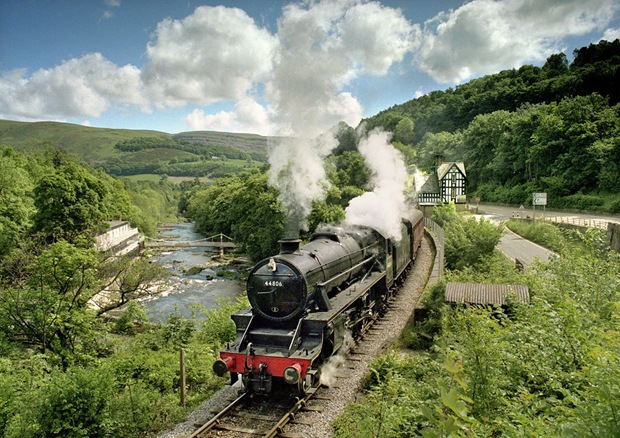 A steam locomotive runs through the green landscape at Berwyn at Denbighshire in Wales, UK 