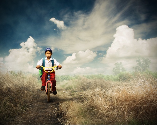 An Indonesian elementary student goes to school with a bike through a barren land.
