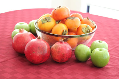 fresh persimmons in a bowl with apples and pomegranates around it.