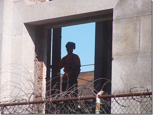 Welder in gutted building looking out at the camera from an empty window opening