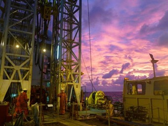 Sunrise over the Greatship Maya's enormous drill. Scientists used the hulking machine to retrieve ancient, fossilized coral from the bottom of the ocean. Credit: ECORD/IODP.