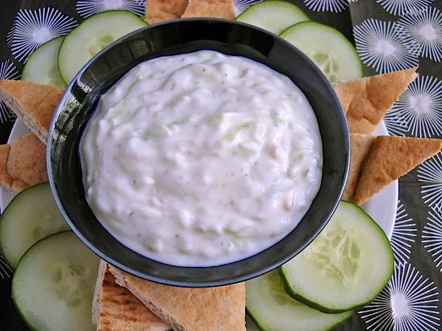 Tzadziki placed in bowl with pita slices and cucumber slices around it 
