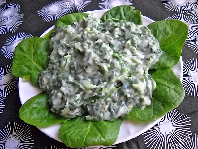 Creamed Spinach on top of leafy greens placed on white plate 