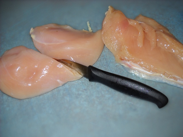 half chicken breasts being cut on cutting board 