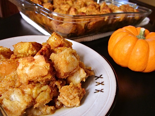 Pumpkin Bread Pudding on white plate with pan of bread pudding in background and staged with mini pumpkin 