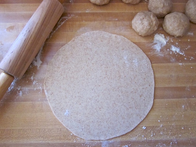 dough balls being rolled out flat with rolling pin 