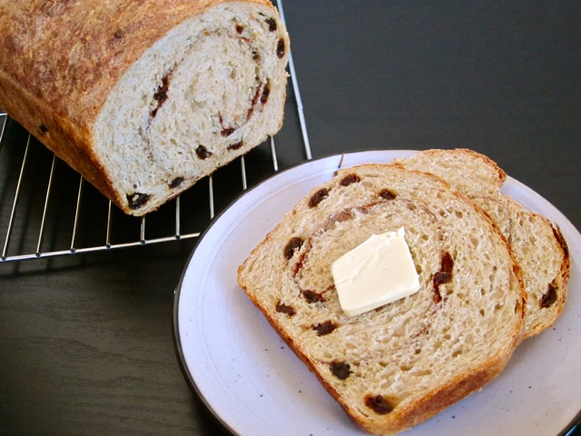 loaf of cinnamon raisin no knead bread with two slices cut and plated on white plate with butter 