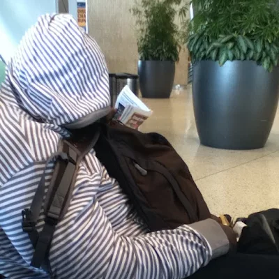 Man sleeping in chair with face covered by stripped sweatshirt with a backpack on his chest and an airline ticket in his hand