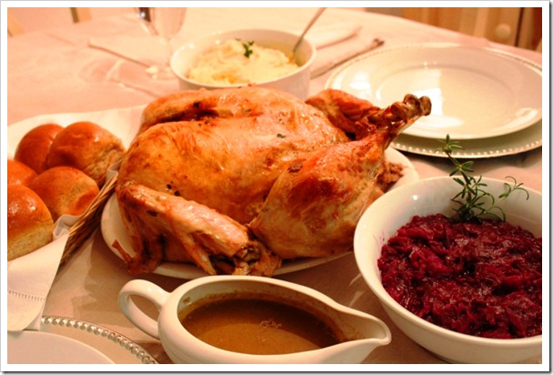 Boneless turkey roast served with a bowl of gravy, basket full of dinner rolls and cranberries 