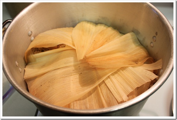 Covering green salsa tamales with corn husks to cook in a large pot