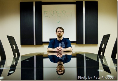 Man sitting at the head of a table with "EXPERT" written on a whiteboard behind him