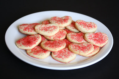 photo of a plate of heart-shaped sugar cookies with red sprinkles