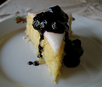 A close up photo of a slice of lemon cornmeal cake topped with blueberry sauce.