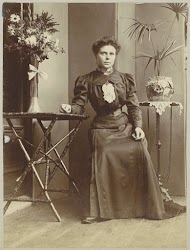 Vrouw zittend in een serre bij tafels met bloemen en planten