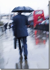 Motion blur image of wet business man with briefcase and umbrella walking to work through the London rain