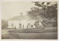 Mannen en jongens in een bloemenperk met een zonnewijzer bij een huis