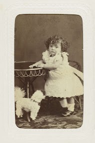 Studioportret van een klein meisje met een speelgoed hondje bij een tafel.