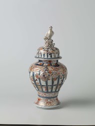 Balustervormige dekselpot met mensen in een interieur achter traliewerk, prunusbomen en bloemranken