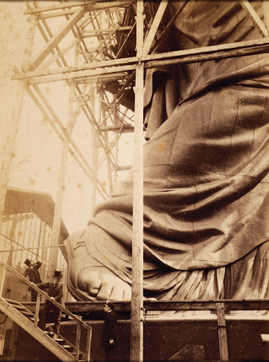 Auguste Bartholdi standing at the foot of the Statue of Liberty