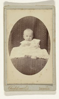 Studioportret van een baby in witte jurk op een stoel