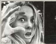 Gezicht van een verschrikt ogende blonde vrouw die tussen de vingers van haar opgeheven hand door kijkt