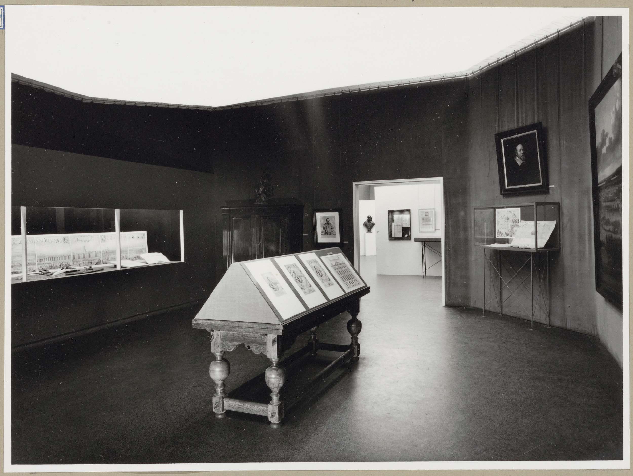 Zaal met een grote vitrine links, een legkast in het midden en een vitrine onder een portret rechts